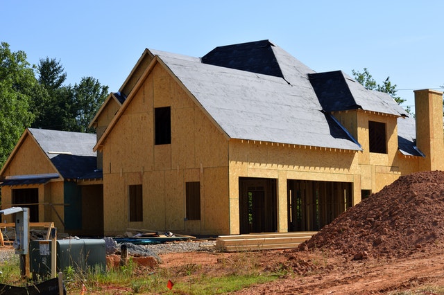Newly constructed custom home in Maryland, featuring wooden framing and black roofing, surrounded by construction materials and a dirt mound.