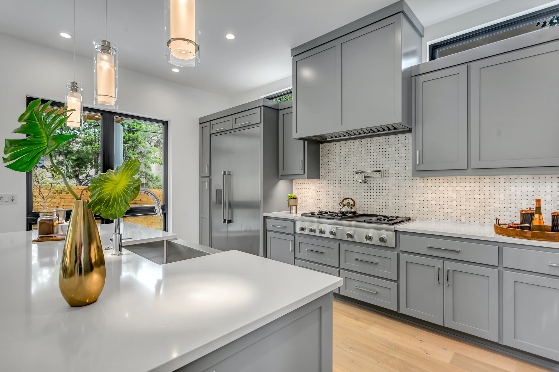 Modern kitchen interior featuring gray cabinetry, stainless steel appliances, and a stylish centerpiece with a green plant in a gold vase, reflecting contemporary design elements relevant to custom home building.